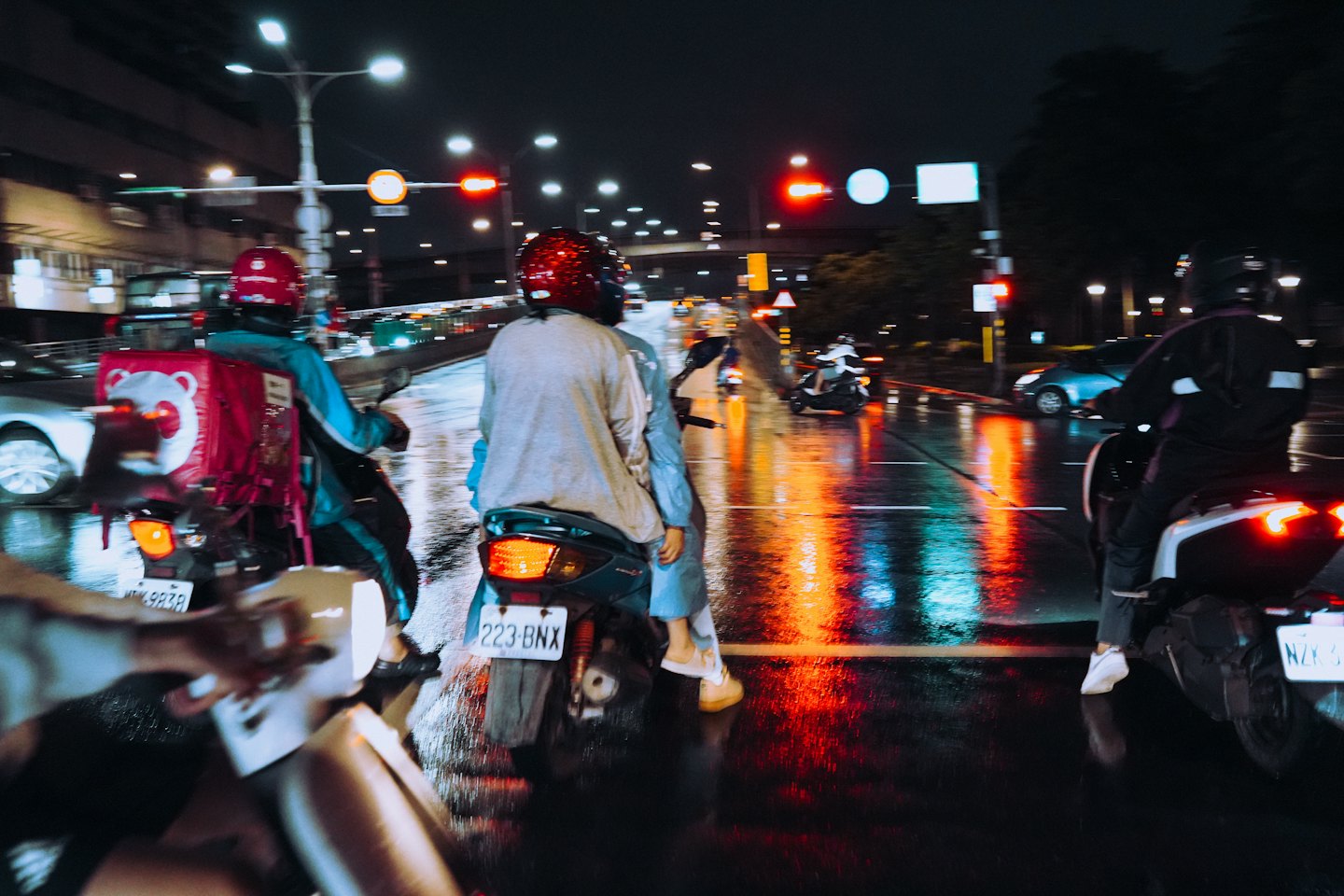 Delivery rider on a scooter carries a pink bag through city traffic.