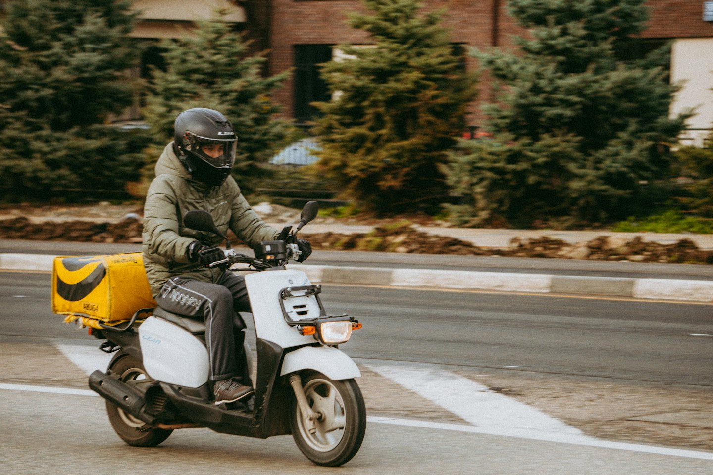 A courier rides a scooter with a yellow delivery box.