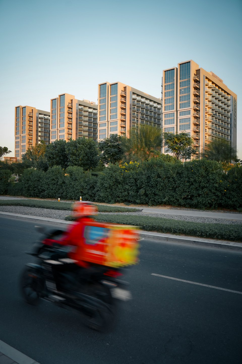 Delivery rider on a motorcycle passing urban apartment buildings.