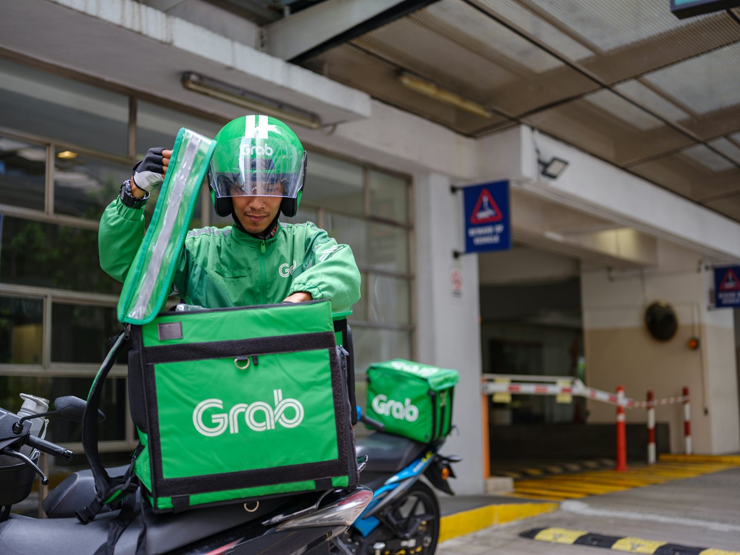Delivery man opens insulated bag on motorcycle in loading bay.